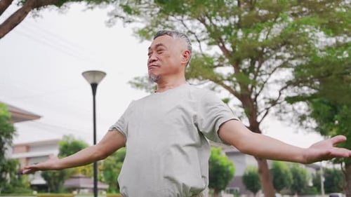 Happy Asian Senior man standing with arms open in a park