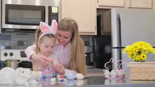 Mother Helping Child Paint Easter Egg in Kitchen