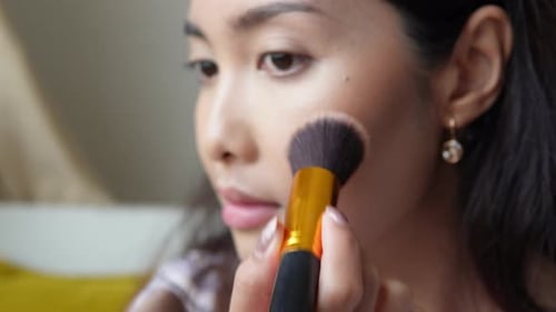 Close up portrait of beautiful young Asian woman applying make up using make up brush and puff
