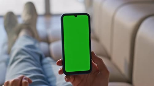 Hand Holding Smartphone with Green Screen on Couch