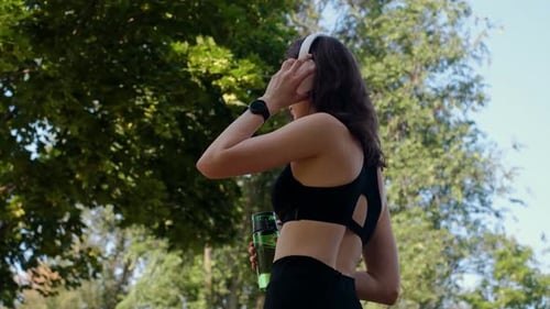Young happy girl doing yoga in the park, listening to music with headphones, sitting in lotus positi