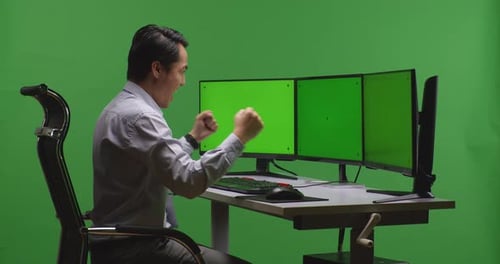 Happy Asian Man Celebrating While Working With Mock Up Multiple Computer Monitor In Green Screen