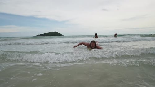 Young active man lying on surfboard and swimming on the beach.