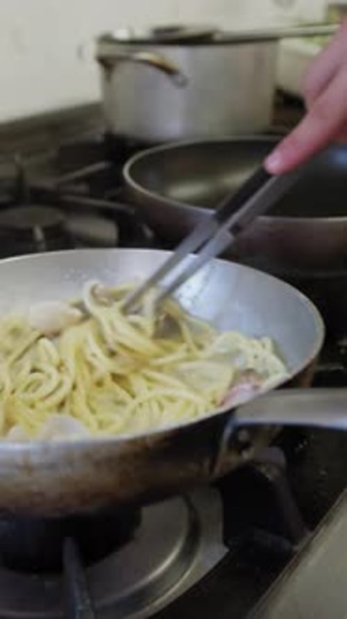 Cuisiner des pâtes spaghettis avec des palourdes dans la poêle d'un restaurant