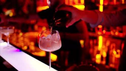 Barman making a cocktail with white sparkling wine at the bar at night with red neon lights, slow mo