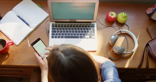 Woman Uses Laptop and Smartphone at Desk