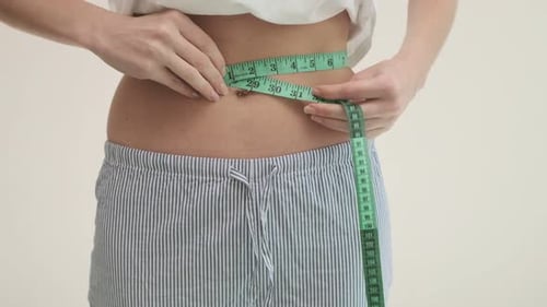 Woman Measures Waist with Measuring Tape Indoors