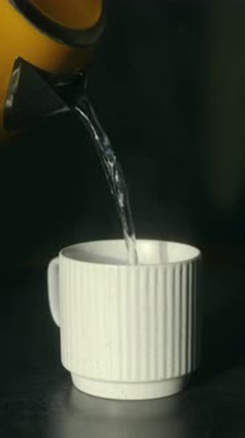 Pouring Water From Kettle Into White Mug