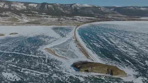 Aerial winter view of Lake Baikal ice and shoreline road near mountains, Russia
