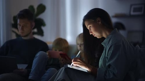 Family Using Digital Devices in Dark Living Room