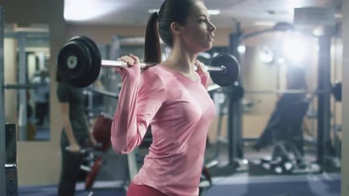 Attractive fit sporty girl is exercising squats with barbell in the gym.