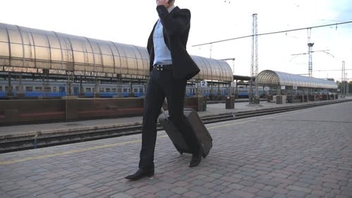 Handsome Businessman Walking Through Railway Station with His Luggage and Talking on phoneYoung