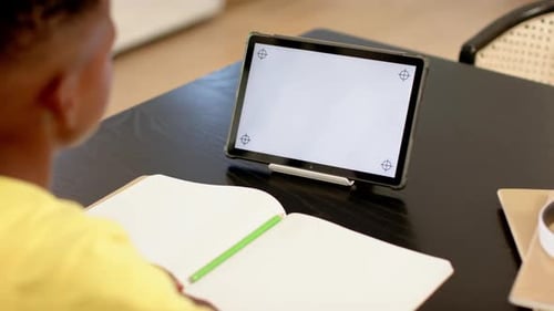 Using tablet and writing in notebook, student studying at school desk, copy space