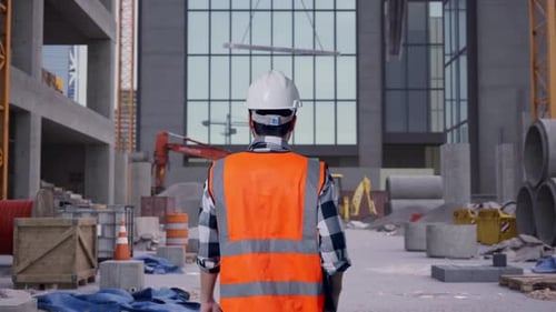 Asian Male Holding Tablet While Walking at Construction Site