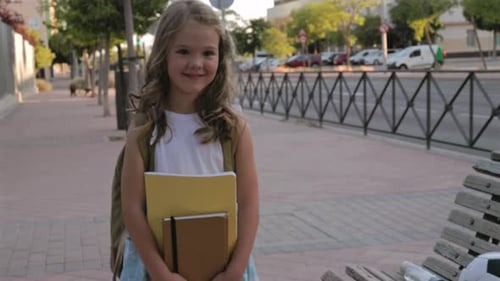 Elementary school student wearing colorful backpack, carrying books and notebook, standing confident