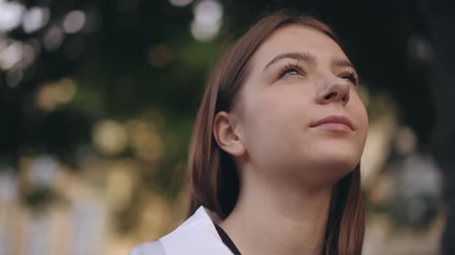 Closeup The Face of a Young Girl Who Looks Up at the Sky and Dreams While Sitting in a City Park on