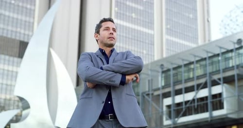 4k video footage of a handsome young businessman posing with his arms folded in the city