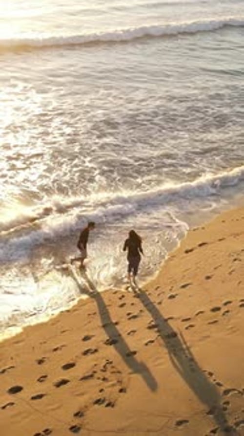 Aerial shot of a couple walking on the beach. Vertical Video.