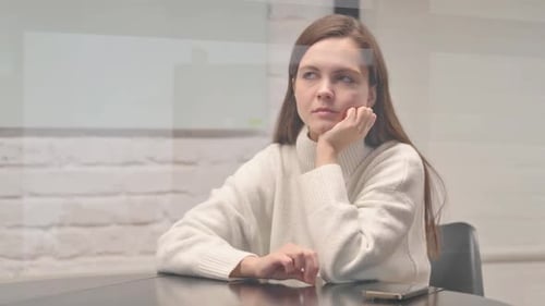 Young Woman Thoughtfully Sitting at Table Indoors