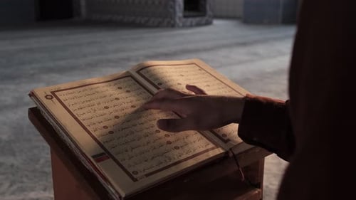 Mann liest das religiöse Buch des Islam, indem er dem Koran mit dem Finger folgt, religiöses Buch mit