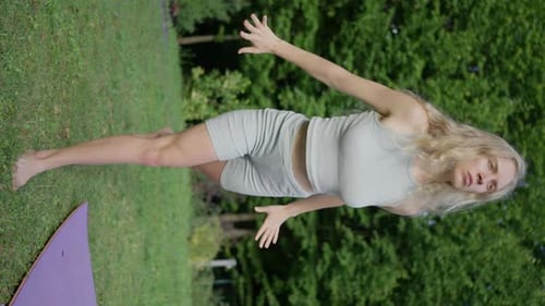 A Blonde Woman Stands on the Grass Performs an Element of Yoga Vertical View