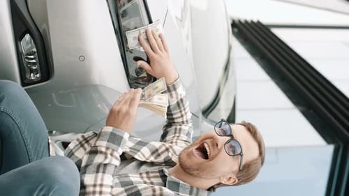 Funny. Happy young man applying money wiping the headlights of the car by american dollar