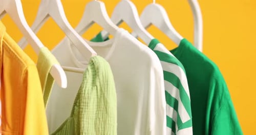 Colorful Clothing on Hangers Displayed Against Yellow Background