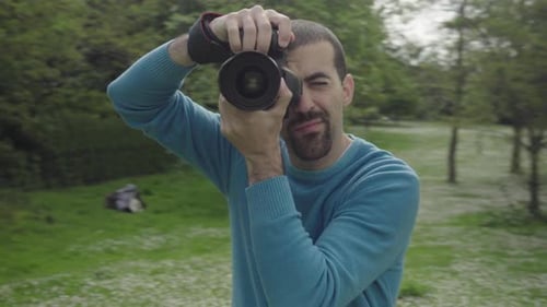 Photographer Taking Photos Of Young Woman On Headphones Listening To Music By A Pond In A Park. S...