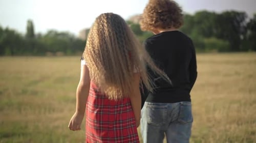 Tracking Shot of Boy and Girl Holding Hands Walking at Sunset on Yellow Meadow in Spring Summer Park