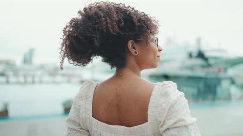 Closeup of a woman in glasses stands in the seaport and looks at the ships