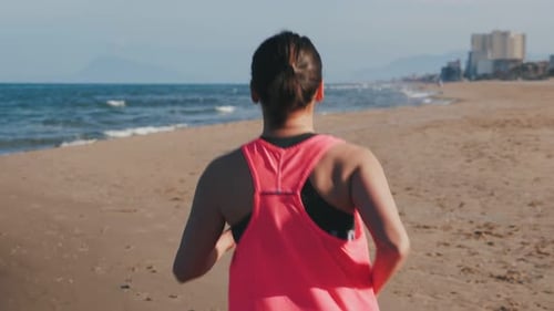 Woman running on beach at sunset. Back follow shot