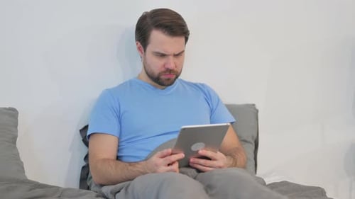Man in Bed Using Tablet Gets Frustrated