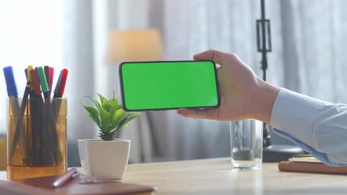 Close up of man's hand holding a mock up green screen smartphone on a desk