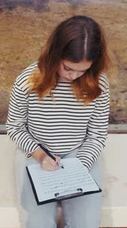 Young Woman Sits and Writes Music Outdoors