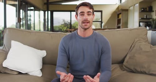 Man Sitting on Sofa Talks and Waves