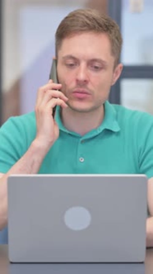 Man Talking on Phone While Working on Laptop