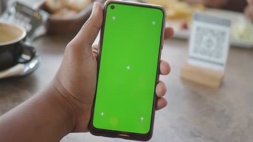 In a Cafe a Hand Holds a Smartphone with a Vibrant Green Screen for Apps Alongside a Beverage