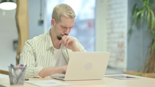 Young Adult Coughs at Laptop in Office