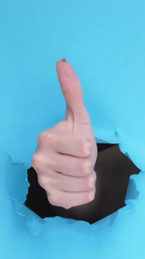 Hand Giving Thumbs Up Through Torn Blue Paper