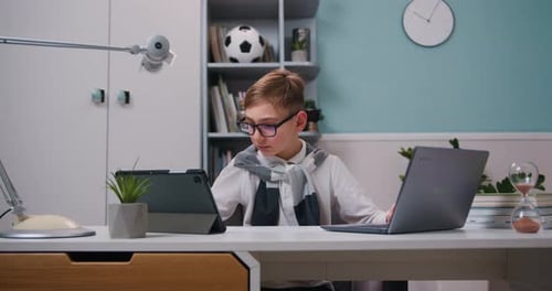 Cute boy is doing homework at table with laptop at home. Kid enjoys making school homework online