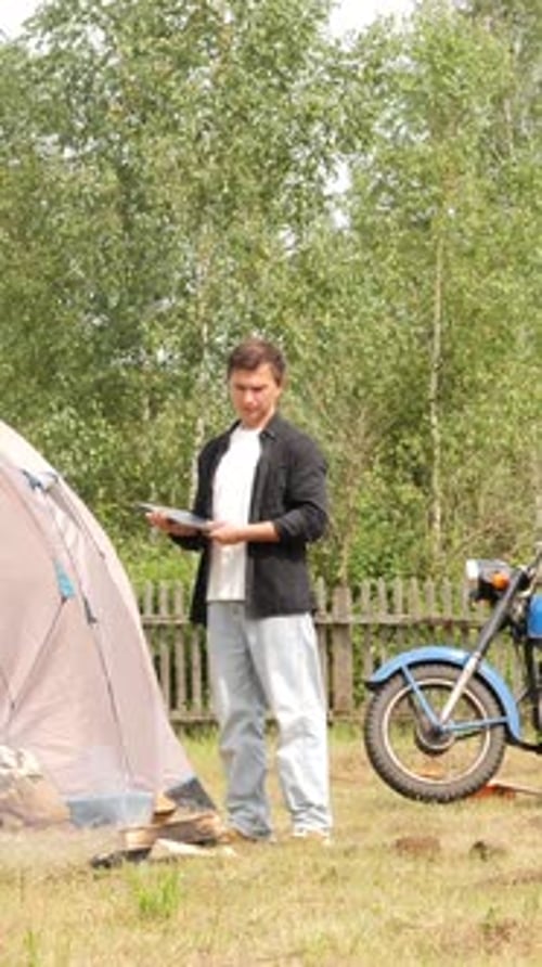Man Camping Opens Laptop near Vintage Motorcycle