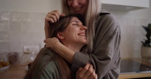 Close Up a Happy Brunette Girl Hugs Her Middleaged Mother Who is Stroking the Girl Hair and Talking