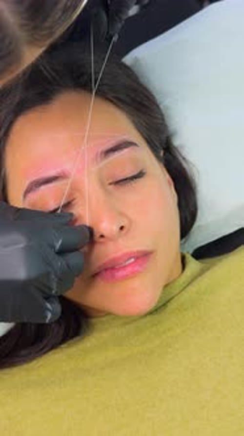 Woman receiving precise eyebrow threading treatment at beauty salon.