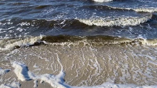 The waves along the seashore slowly rolling in over the sand.