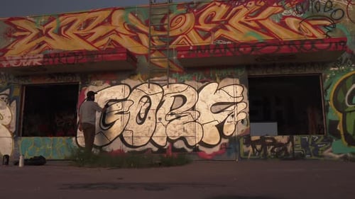 Jovem macho pulverizando grafite na parede do prédio abandonado