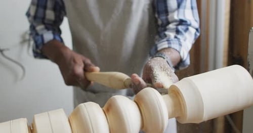 African american male carpenter wearing protective helmet turning wood on a lathe at carpentry shop