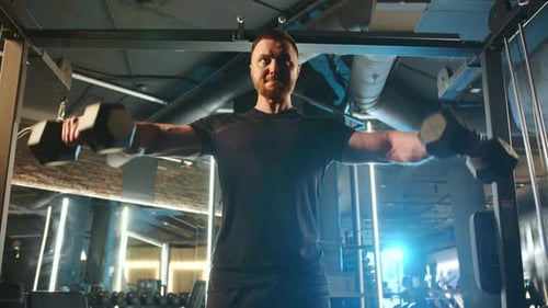 Man Does Dumbbell Lateral Raises for Shoulder Workout in a Gym Showing Strength and Determination