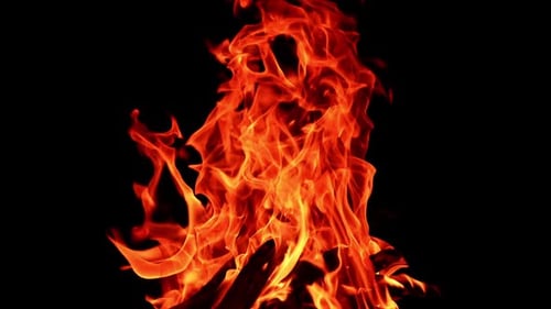 Rather large campfire burning at night. Fire flames lean to the side and tiny sparkles rise up.