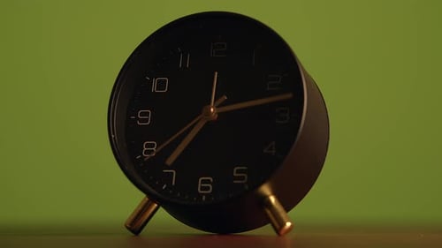 Un elegante despertador negro colocado sobre un fondo verde vibrante para un atractivo estético