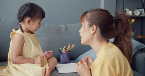 mom teach girl paint use album and colourful pencils having fun relax on couch in living room.